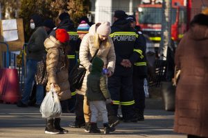 Ukrainian refugee family of mother and two children, stand in front of backdrop of Romanian emergency workers at a transit centre for Ukrainians