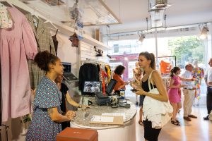 customer talks to cashier in charity shop while people in background stand and talk