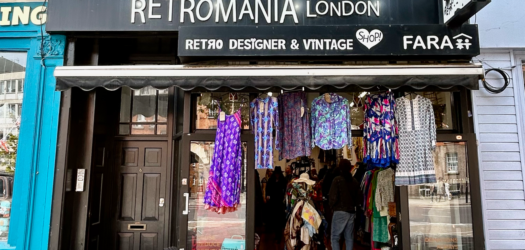 Exterior of Retromania London, a FARA charity shop selling retro, designer, and vintage clothing, with colorful garments displayed at the entrance under a black shop sign.