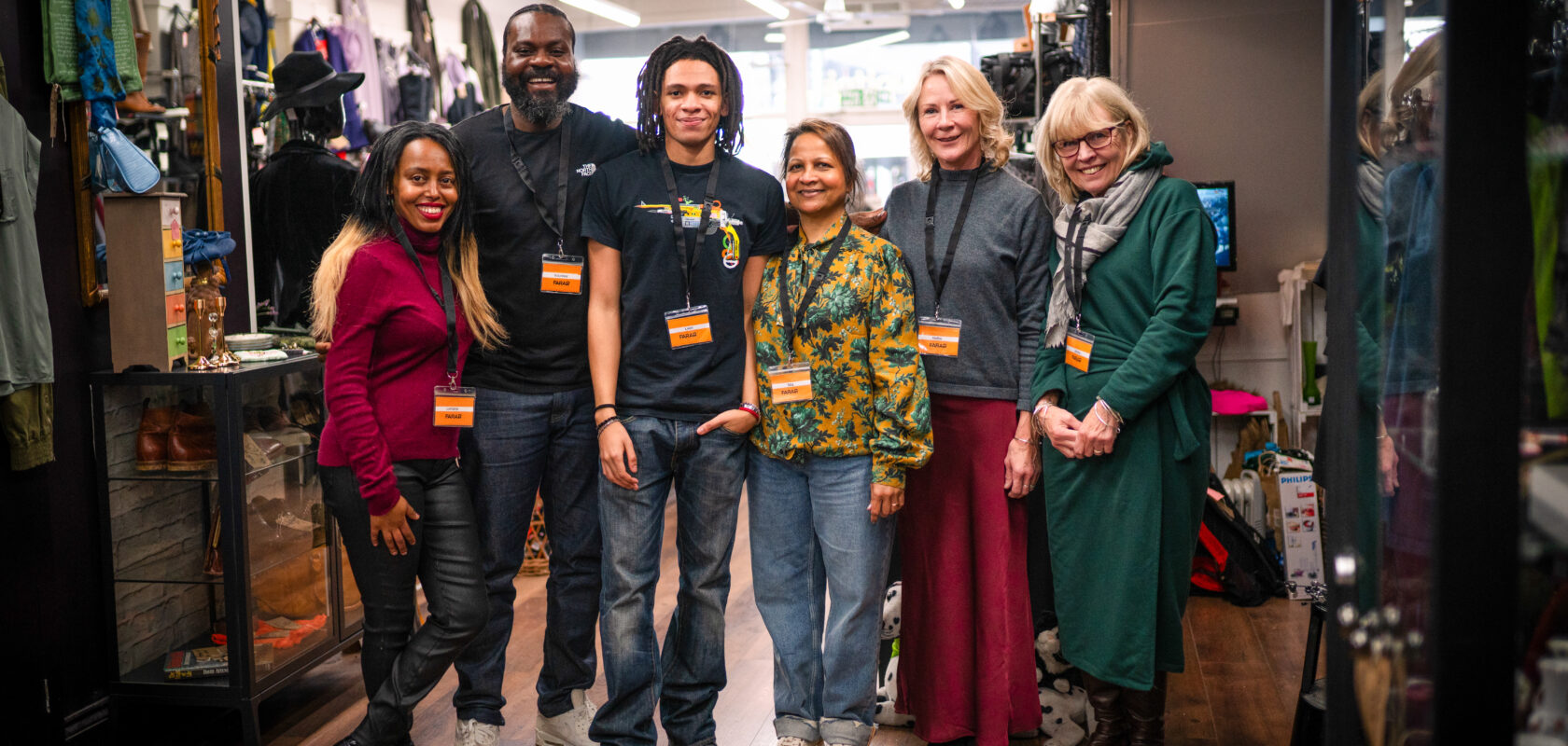 ChatGPT said:
A group of six FARA staff and volunteers stand together inside a brightly lit charity shop, smiling at the camera. They are wearing name badges and lanyards, surrounded by neatly displayed clothing and accessories.