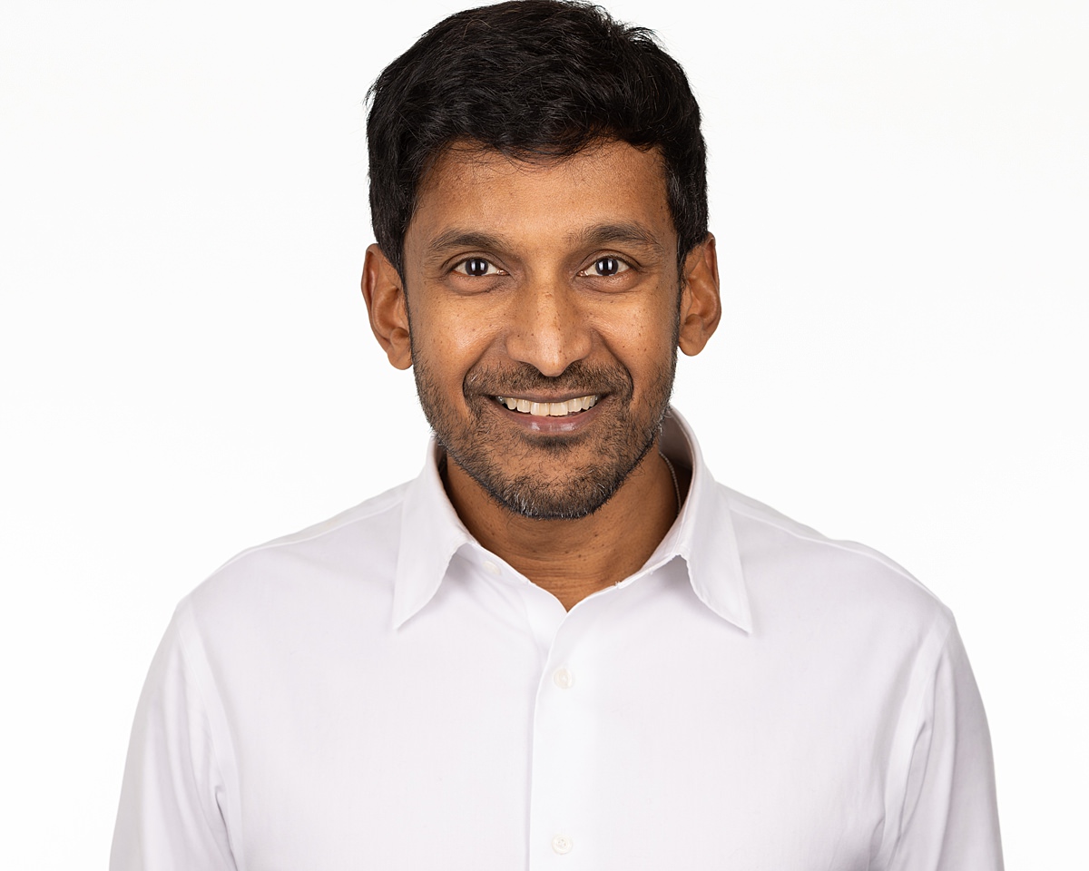 A headshot style photo Paul Gunaratnam wearing a white shirt and and smiling directly at the camera