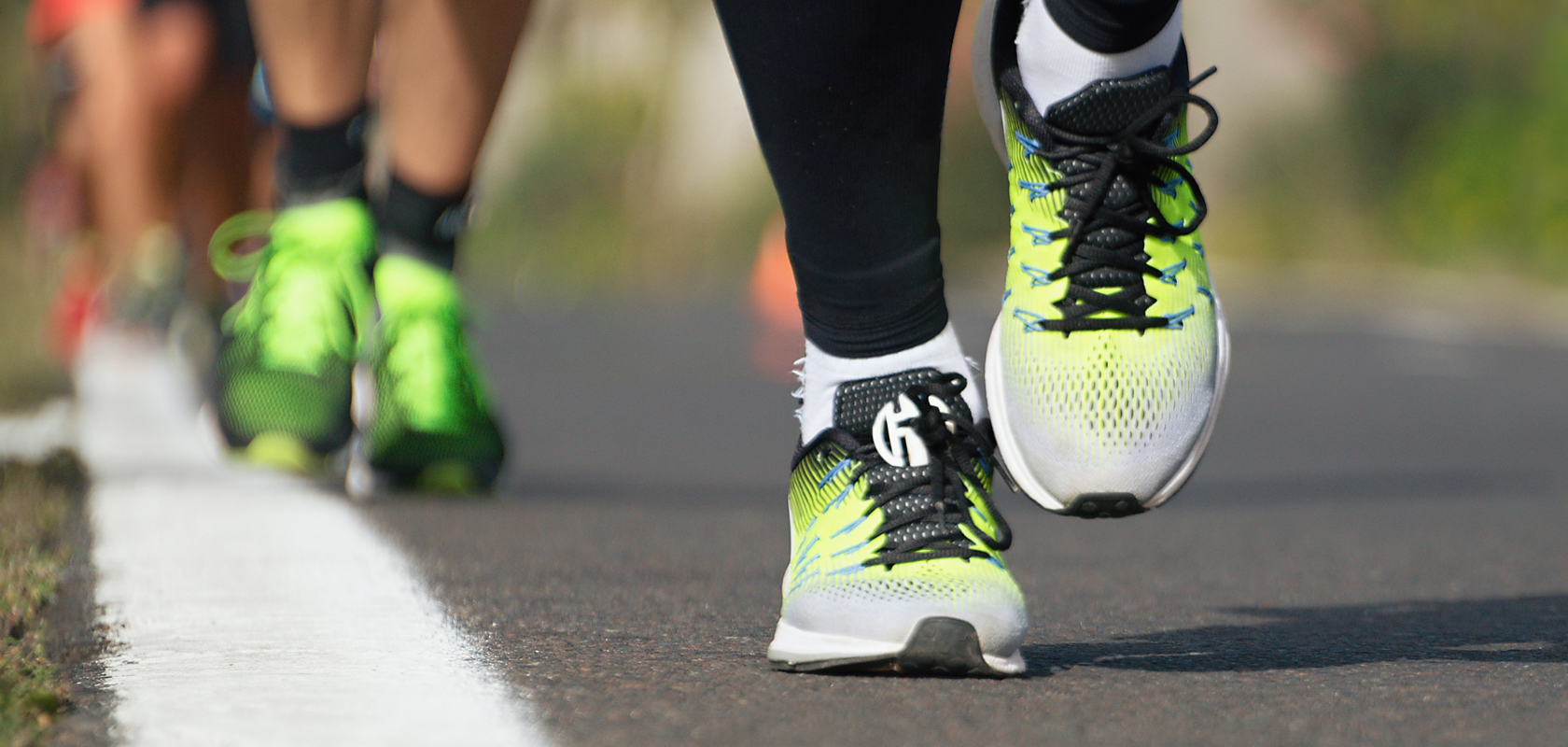 closeup of someone's feet whilst running on a road. They are wearing, green and black running trainers